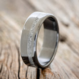 Shown here is "Vertigo", a custom, handcrafted men's wedding ring featuring an offset moonstone inlay on a fire-treated black zirconium band, upright facing left. Additional inlay options are available upon request.