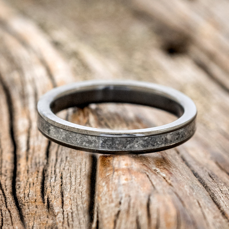 Shown here is "Perenna", a custom, handcrafted women's stacking band featuring a crushed moonstone inlay on a fire-treated black zirconium band, laying flat. Additional inlay options are available upon request.