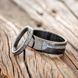 Shown here is a matching wedding band set featuring "Vertigo" and "Perenna", laying together. "Vertigo" is a handcrafted wide wedding band featuring an offset crushed moonstone inlay. "Perenna" is a stacking-style wedding band featuring a crushed moonstone inlay. Both rings are shown on fire-treated black zirconium bands.