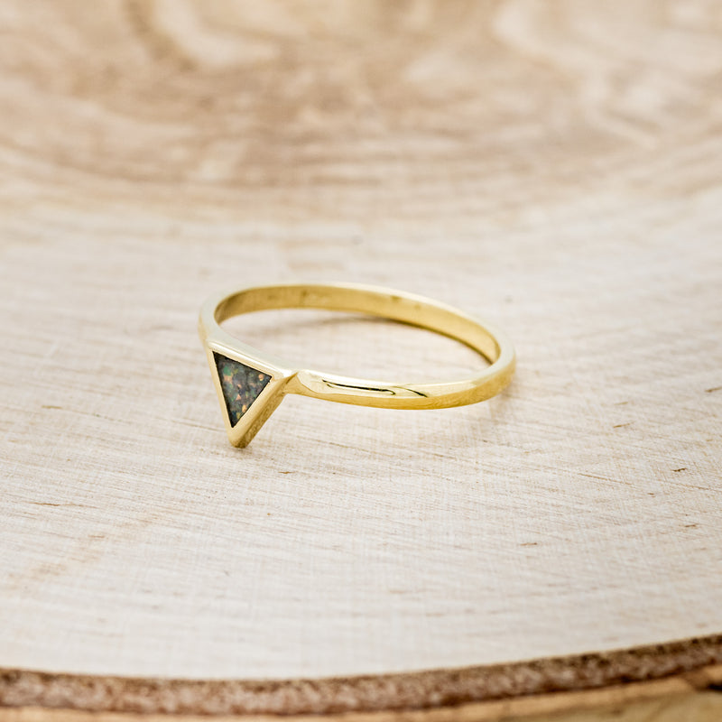 Shown here is "Mera", a triangle-style women's stacking band featuring a triangle channel filled with black fire opal on a 14K gold band, facing left. Many center stone options are available upon request.