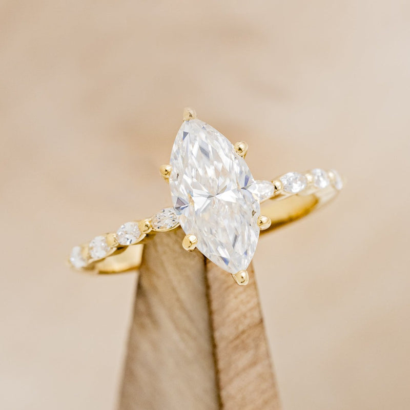 Shown here is "Romy", a marquise moissanite women's engagement ring with diamond accents, on stand tilted right. Many other center stone options are available upon request.