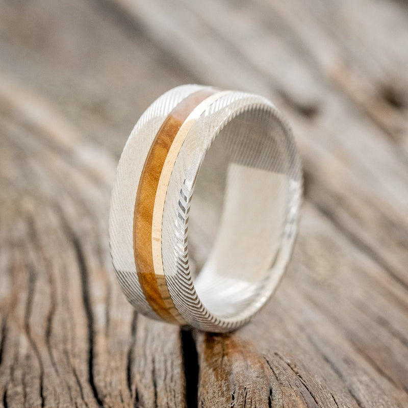 Shown here is "Asher", a custom, handcrafted men's wedding ring featuring a Bethlehem olive wood and a 14K yellow gold inlay on a Damascus steel band, upright facing left. Additional inlay options are available upon request.