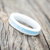 Shown here is "Perenna", a custom, handcrafted women's stacking band featuring a turquoise inlay on a white ceramic band, tilted left. Additional inlay options are available upon request.