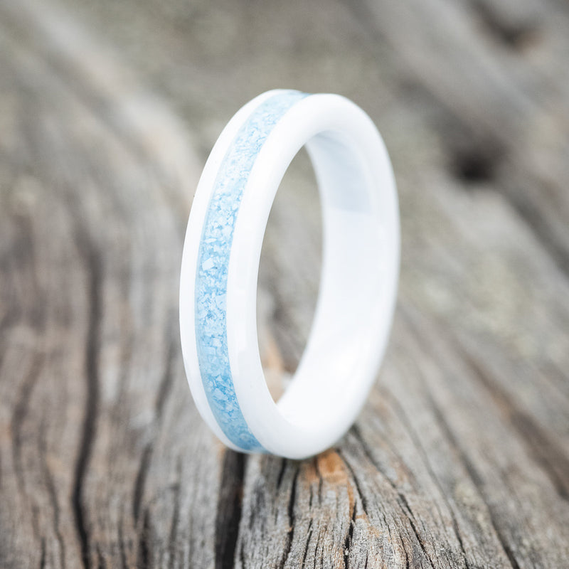 Shown here is "Perenna", a custom, handcrafted women's stacking band featuring a turquoise inlay on a white ceramic band, upright facing left. Additional inlay options are available upon request.