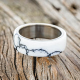 Shown here is "Haven", a custom, handcrafted men's wedding ring featuring a white turquoise TruStone overlay on a titanium band, laying flat. Additional overlay options are available upon request.