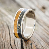 Shown here is "Dyad", a custom, handcrafted men's wedding ring featuring 2 channels with whiskey barrel oak and black and gold matrix TruStone inlays, upright facing left. Additional inlay options are available upon request.