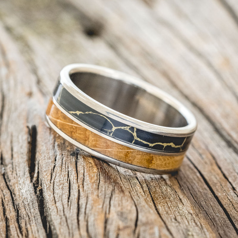 Shown here is "Dyad", a custom, handcrafted men's wedding ring featuring 2 channels with whiskey barrel oak and black and gold matrix TruStone inlays, tilted left. Additional inlay options are available upon request.