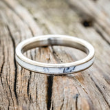 Shown here is "Eterna", a custom, handcrafted wedding ring featuring white turquoise TruStone overlay on a titanium band, laying flat. Additional inlay options are available upon request.