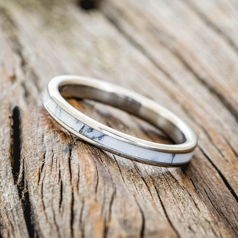 Shown here is "Eterna", a custom, handcrafted wedding ring featuring white turquoise TruStone overlay on a titanium band, tilted left. Additional inlay options are available upon request.