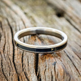 Shown here is "Eterna", a custom, handcrafted wedding ring featuring black and gold matrix TruStone inlay on a titanium band, laying flat. Additional inlay options are available upon request.
