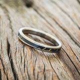 Shown here is "Eterna", a custom, handcrafted wedding ring featuring black and gold matrix TruStone inlay on a titanium band, tilted left. Additional inlay options are available upon request.