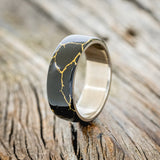 Shown here is "Haven", a custom, handcrafted wedding ring featuring black and gold matrix TruStone overlay on a titanium band, upright facing left. Additional inlay options are available upon request.