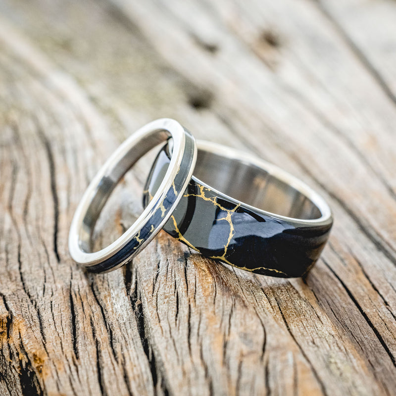 Shown here is "Haven" & "Eterna", custom, handcrafted matching set of wedding rings featuring black and gold matrix TruStone overlay on titanium bands, laying together. Additional inlay options are available upon request.