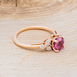 Shown here is "Blossom", a round cut lab-created ruby women's engagement ring with leaf-shaped diamond accents, facing right. Many other center stone options are available upon request.
