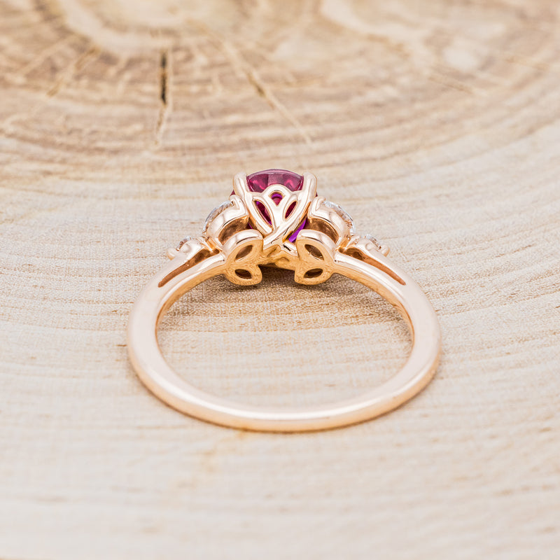 Shown here is "Blossom", a round cut lab-created ruby women's engagement ring with leaf-shaped diamond accents, back view. Many other center stone options are available upon request.