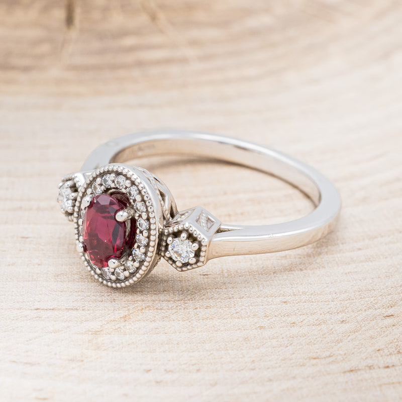 Shown here is "Amelia", a vintage-style lab-created ruby women's engagement ring with a diamond halo and diamond accents, facing left. Many other center stone options are available upon request.