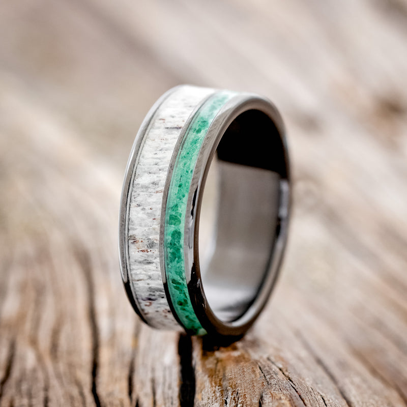 Shown here is "Raptor", a custom, handcrafted men's wedding ring featuring a malachite & antler inlay, shown here set on a black zirconium band, upright facing left. Additional inlay options are available upon request.