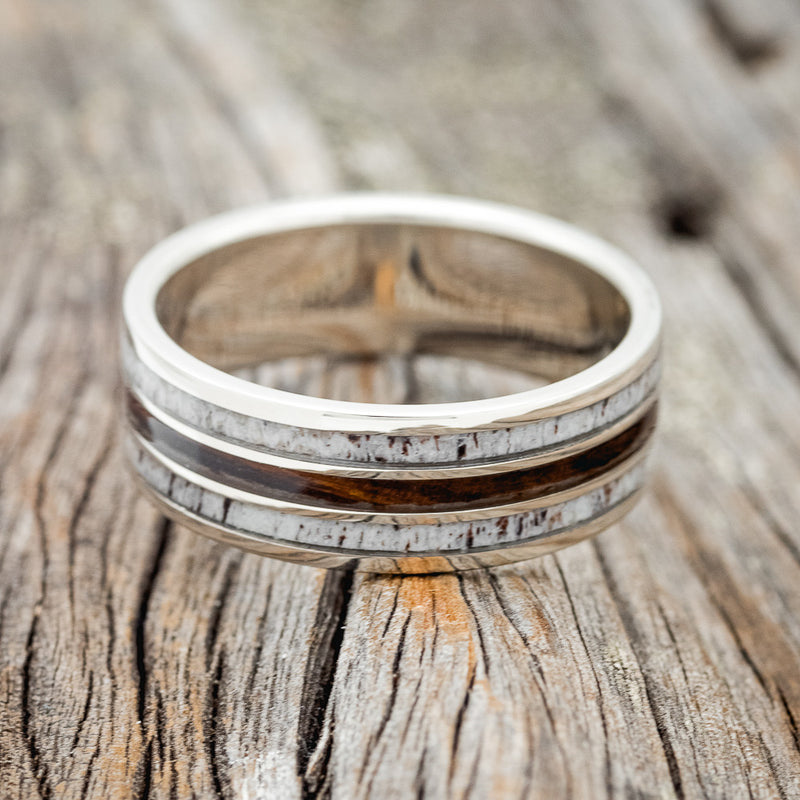 Shown here is "Rio", a custom, handcrafted men's wedding ring featuring 3 channels with ironwood and antler inlays, laying flat. Additional inlay options are available upon request.