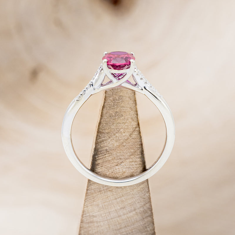 Shown here is "Roslyn", an oval lab-created ruby women's engagement ring with diamond accents, side view on stand. Many other center stone options are available upon request.