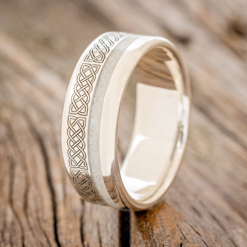 Shown here is "Vertigo", a custom engraved Celtic sailor's knot-patterned men's wedding ring featuring a fire and ice opal inlay, upright facing left. Additional inlay options are available upon request.