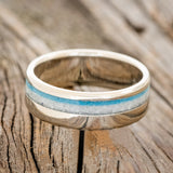 Shown here"Castor" is a custom, handcrafted men's wedding ring featuring a white buffalo turquoise and turquoise inlay on a 14K gold band, laying flat.