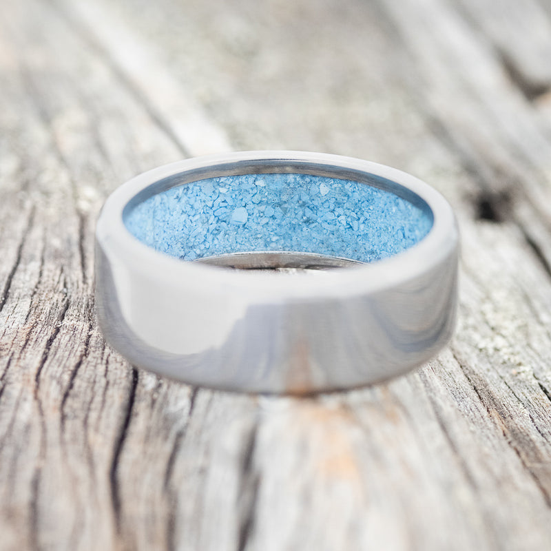 Shown here is a handcrafted men's wedding ring featuring hand-crushed turquoise on any of our available base material options, laying flat. Additional inlay options are available upon request.