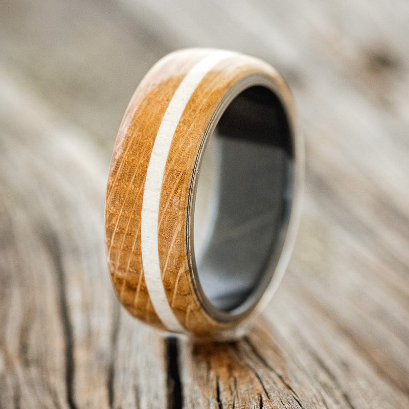 Shown here is "Remmy", a custom, handcrafted men's wedding ring featuring an authentic whiskey barrel wood overlay and an elk antler inlay, upright facing left. Additional inlay options are available upon request.