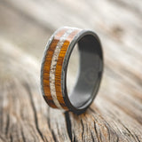 Shown here is "Rainier", a custom, handcrafted men's wedding ring featuring an  ironwood and antler inlay on a hammered, fire-treated black zirconium band, upright facing left. Additional inlay options are available upon request.