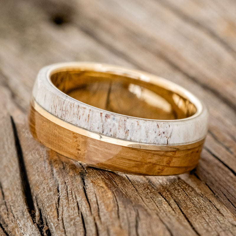 Shown here is "Golden", a handcrafted men's wedding ring featuring a whiskey barrel and antler overlay with a 14K yellow gold inlay, tilted left. Additional inlay options are available upon request.