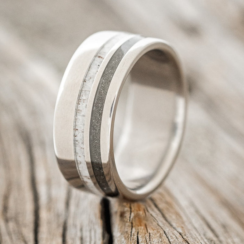 Shown here is "Cosmo", a custom, handcrafted men's wedding ring featuring iron ore and antler inlays on a titanium band, upright facing left. Additional inlay options are available upon request.