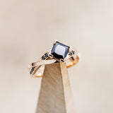 Shown here is "Lina", a black moissanite women's engagement ring with black diamond accents, on stand facing slightly right. Many other center stone options are available upon request.