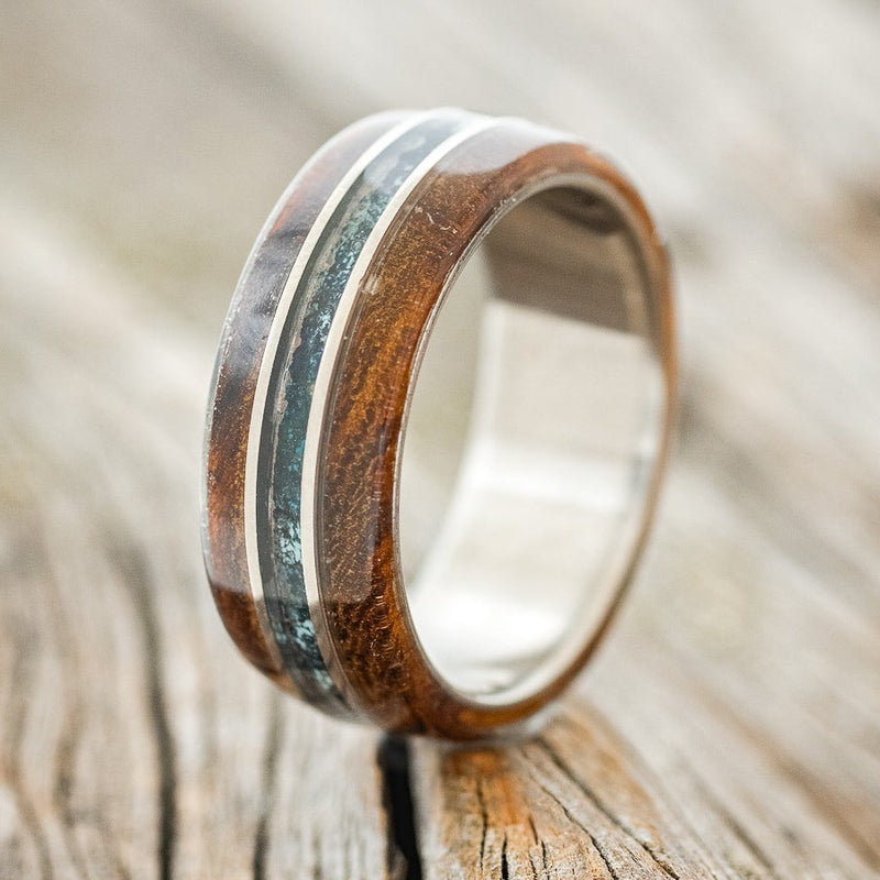 Shown here is "Glen", a custom, handcrafted men's wedding ring featuring ironwood overlays and a patina copper inlay, upright facing left. Additional inlay options are available upon request.