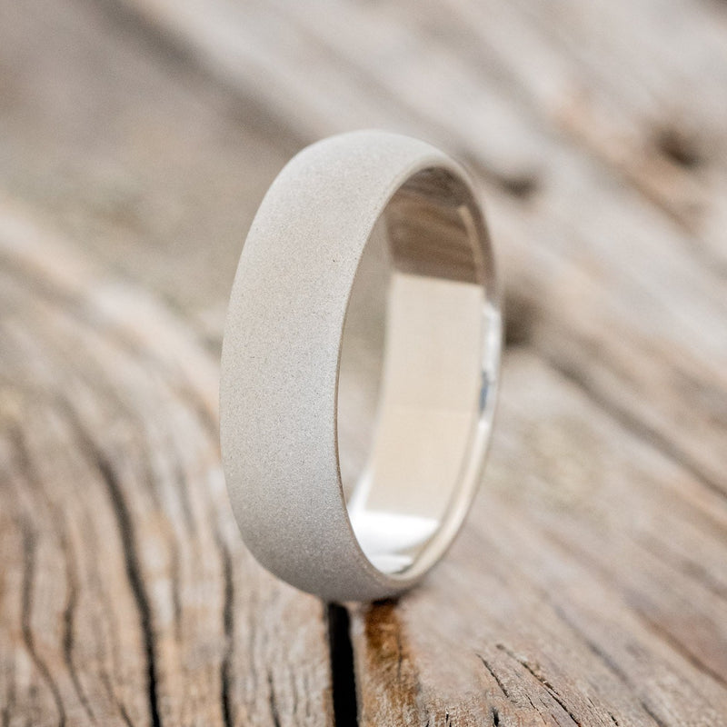 Shown here is a handcrafted men's wedding ring featuring a domed profile and sandblasted finish, upright facing left. Additional inlay options are available upon request.