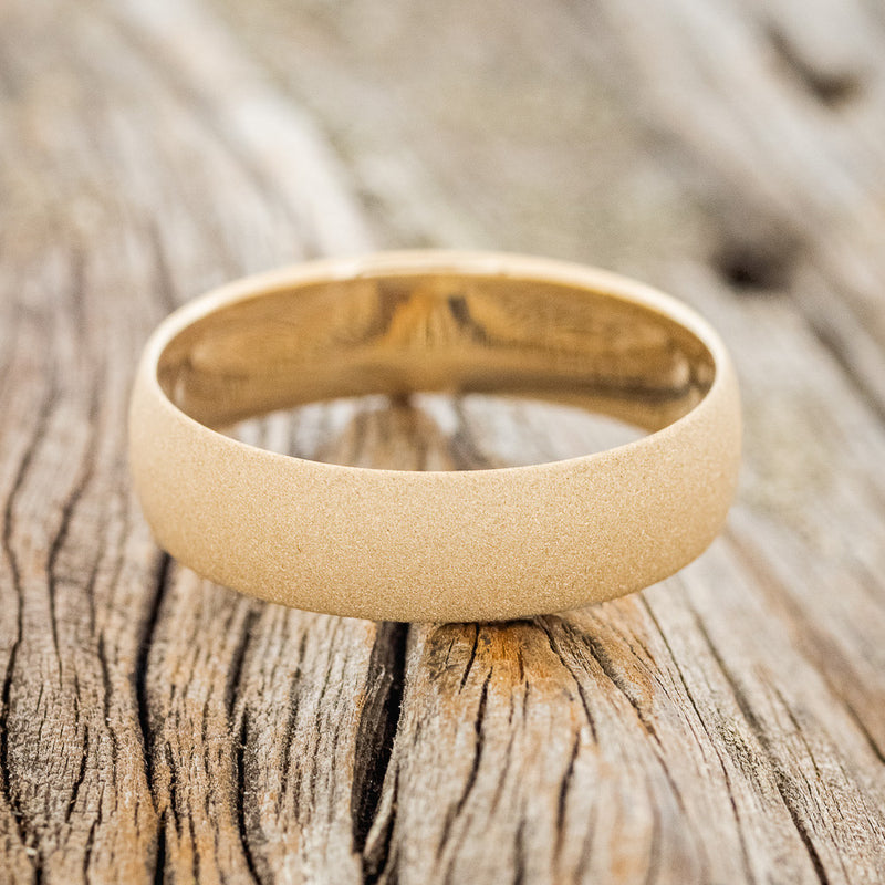 Shown here is a handcrafted men's wedding ring featuring a domed profile and sandblasted finish, laying flat. Additional inlay options are available upon request.