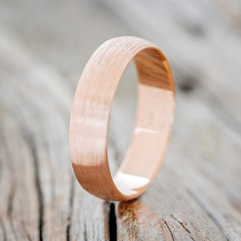 Shown here is a custom, handcrafted wedding band featuring a domed 14K gold band with a brushed finish, upright facing left. Additional inlay options are available upon request.
