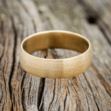 Shown here is a custom, handcrafted wedding band featuring a domed 14K gold band with a brushed finish, laying flat. Additional inlay options are available upon request.
