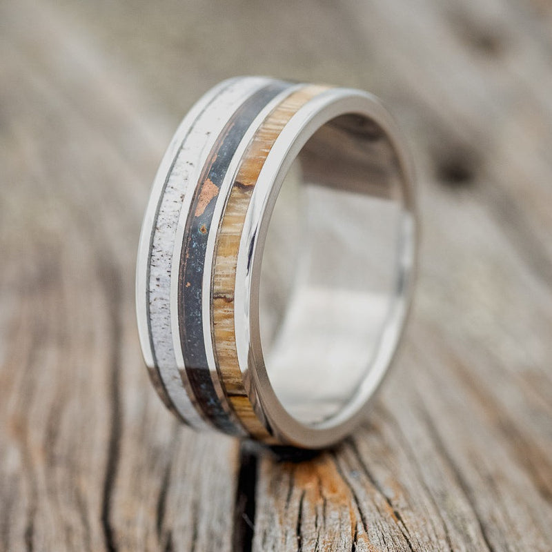 Shown here is "Rio", a custom, handcrafted men's wedding ring featuring 3 channels with elk antler, patina copper, and spalted maple inlays on a titanium band, upright facing left. Additional inlay options are available upon request.