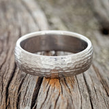 Shown here is a handcrafted men's wedding ring featuring a solid band with a domed profile and hammered finish, laying flat. Additional inlay options are available upon request.
