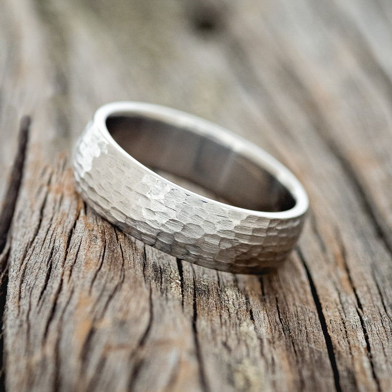 Shown here is a handcrafted men's wedding ring featuring a solid band with a domed profile and hammered finish, tilted left. Additional inlay options are available upon request.