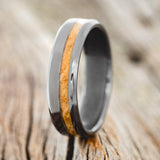 Shown here is "Vertigo", a custom, handcrafted men's wedding ring featuring an offset whiskey barrel inlay, shown here on a fire-treated black zirconium band, upright facing left. Additional inlay options are available upon request.