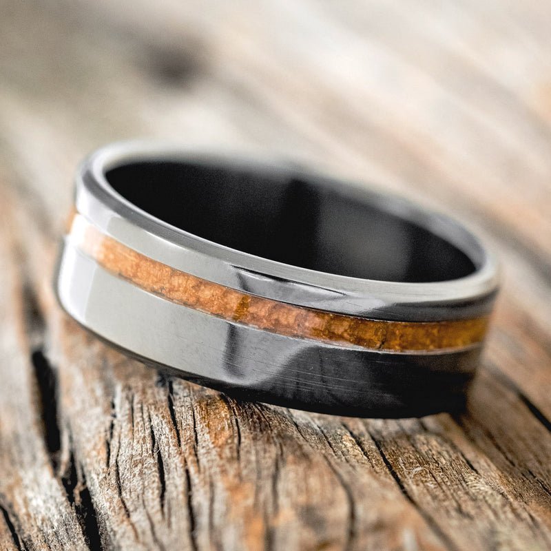 Shown here is "Vertigo", a custom, handcrafted men's wedding ring featuring a whiskey barrel inlay, shown here on a fire-treated black zirconium band, tilted left. Additional inlay options are available upon request.
