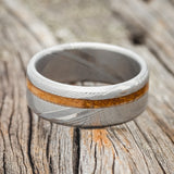 Shown here is "Vertigo", a custom, handcrafted men's wedding ring featuring a whiskey barrel inlay, shown here on a Damascus steel band, laying flat. Additional inlay options are available upon request.