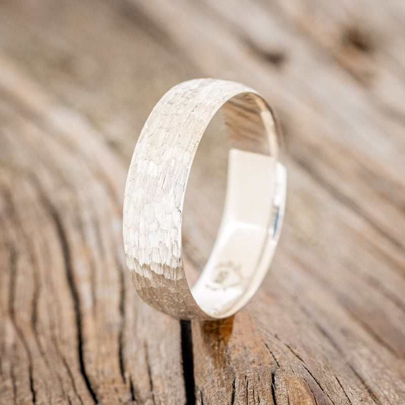 Shown here is a handcrafted men's wedding ring featuring a solid band with a domed profile and hammered finish, upright facing left. Additional inlay options are available upon request.