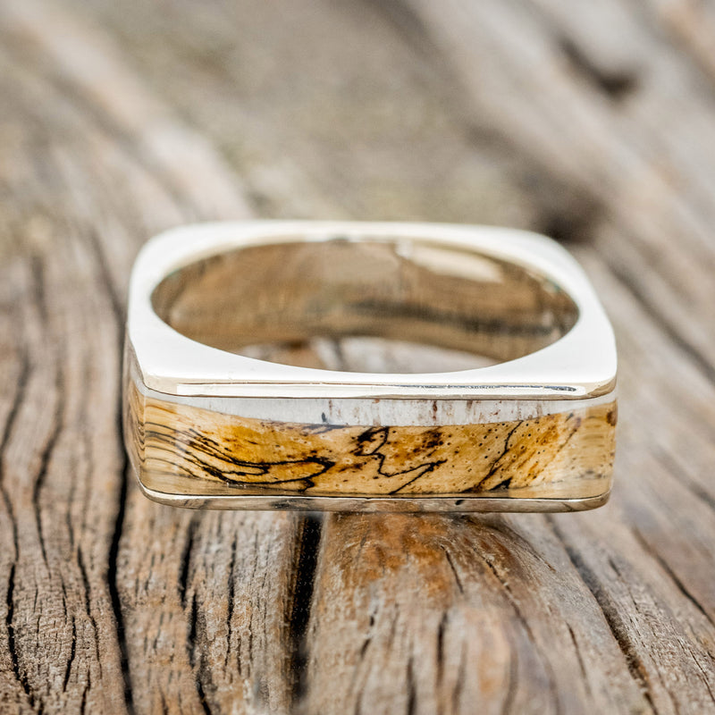 Shown here is "Mesa", a custom, handcrafted men's wedding band featuring a 14K gold band with an elk antler and spalted maple inlay, laying flat. Additional inlay options are available upon request.