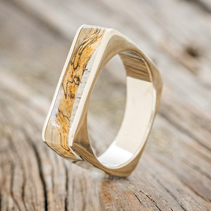 Shown here is "Mesa", a custom, handcrafted men's wedding band featuring a 14K gold band with an elk antler and spalted maple inlay, upright facing left. Additional inlay options are available upon request.