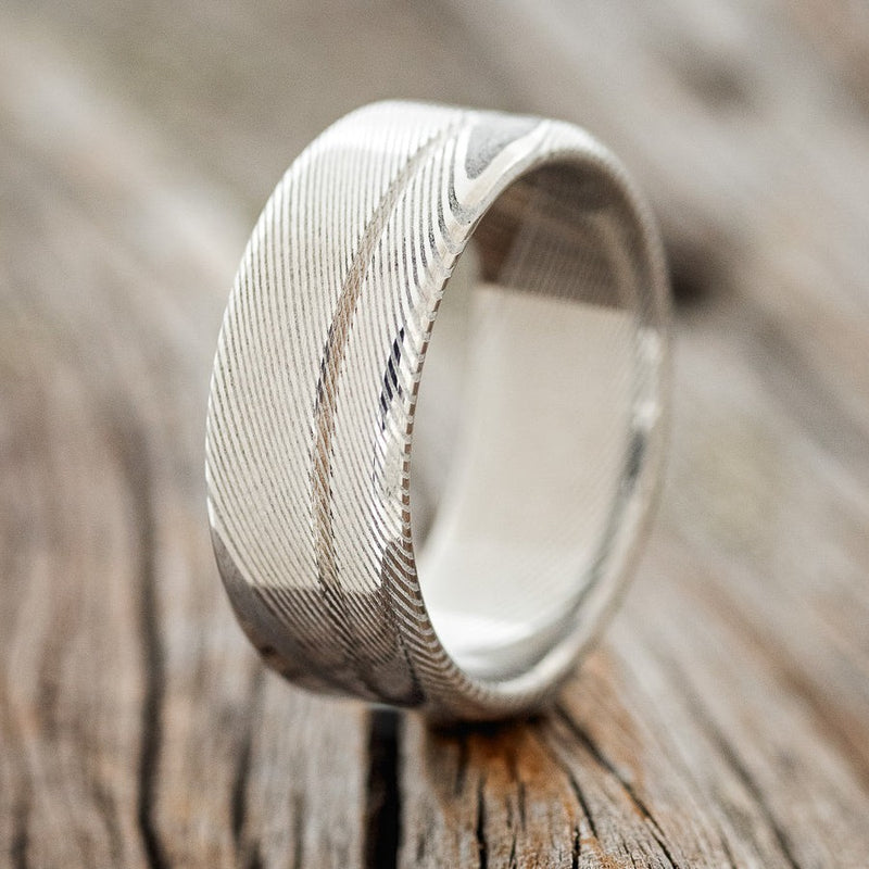 Shown here is a handcrafted men's wedding ring featuring a solid Damascus steel band with an offset etched groove, upright facing left. Additional inlay options are available upon request.