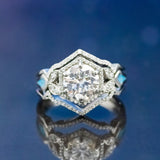 Shown here is The "Lucy in the Sky", a halo-style moissanite women's engagement ring with delicate and ornate details and is available with many center stone options, and is shown with turquoise inlays on both sides.