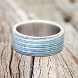 Shown here is a custom, handcrafted men's wedding ring featuring a threaded pattern with turquoise inlays, laying flat. Additional inlay options are available upon request.