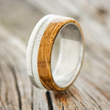 Shown here is "Ezra", a custom, handcrafted men's wedding ring featuring a whiskey barrel oak and antler overlay on a Damascus steel band, upright facing left. Additional inlay options are available upon request.