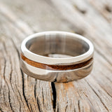 Shown here is "Vertigo", a custom, handcrafted men's wedding ring featuring a koa wood inlay, laying flat. Additional inlay options are available upon request.